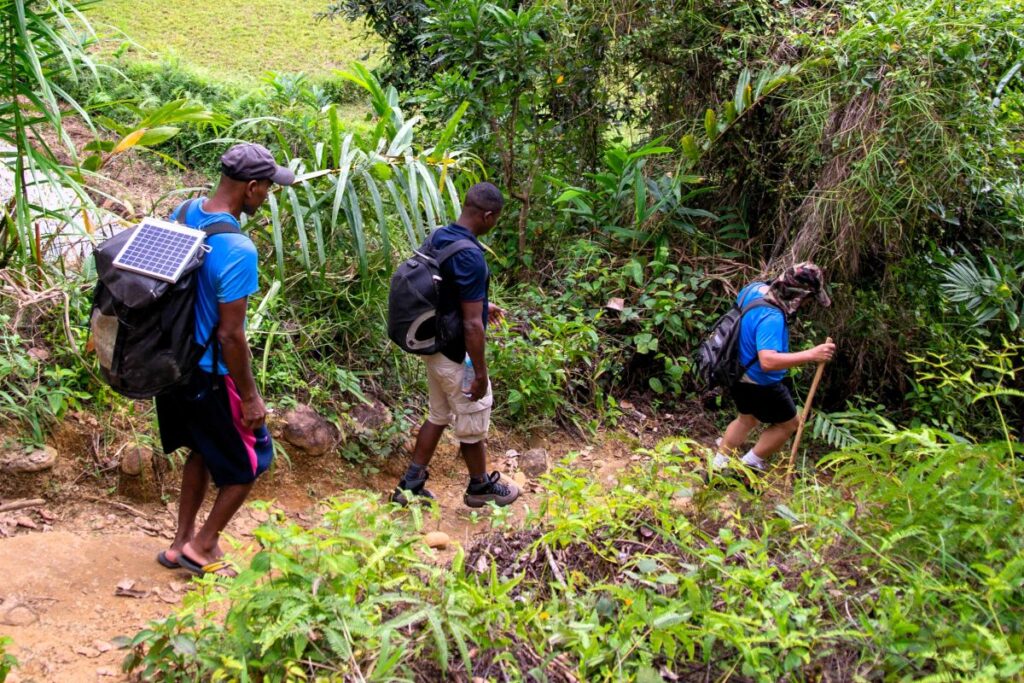 Three men hike down a narrow trail.